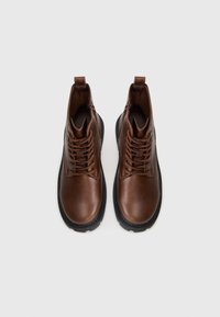 Bruna läderstövlar med texturerad yta, snörning framtill och dragkedja på sidan. Svart gummisula med en något upphöjd kant.