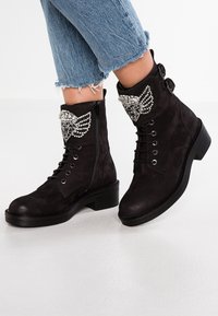 Botas de tobillo de ante negro con un acabado texturizado, con un acento decorativo de strass en el puño, y con cordones resistentes y detalle de cremallera.