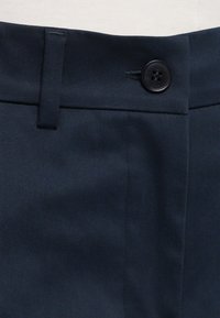 Tissu bleu marine avec une ceinture dotée d'un unique bouton noir et une boucle de ceinture sur un pantalon.