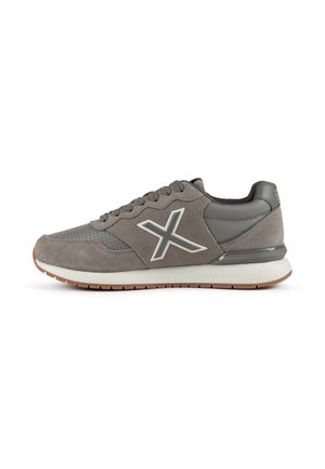 Zapatilla gris de ante y cuero con cordones, suela blanca, suela marrón y un logo "X" con contorno blanco en el lateral.