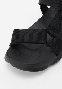 Svarte sandaler med justerbare nylonremmer, en teksturert gummisåle og en polstret såle med et mønstret overflate for grep.