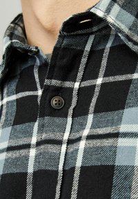 Camisa de franela de cuadros en negro y azul con cierre de botones, que presenta una textura suave, un patrón de cuadros prominente y un collar doblado.