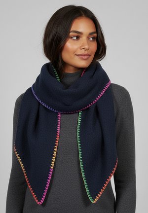 Woman wearing dark navy scarf with rainbow-colored stitched edges over a gray textured sweater, looking to the side with a slight smile.