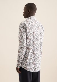 Langsleeve shirt van witte stof met een levendige bloemenprint in tinten van blauw, rood en groen. Klassieke kraag en afgeronde zoom.