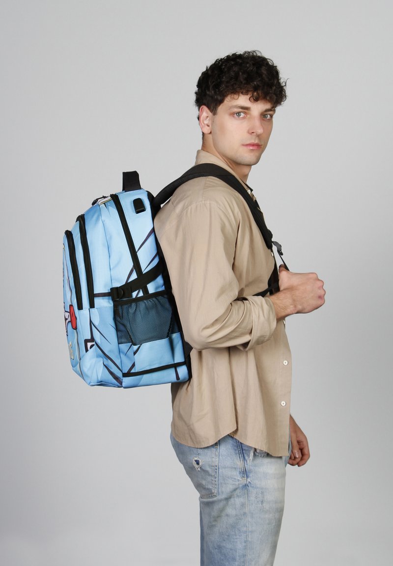 Mochila azul con detalles en negro, múltiples compartimentos y un diseño de dibujos animados. El modelo la lleva sobre un hombro frente a un fondo liso.