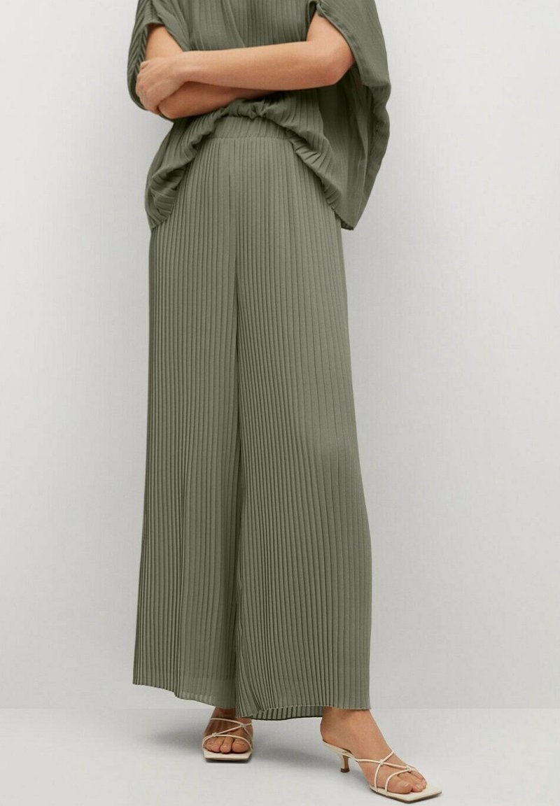 Pantalons larges plissés de couleur vert olive, fabriqués en tissu léger, associés à des sandales beiges à lanières. Design simple, fluide et coupe décontractée.