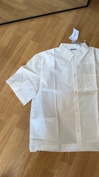 Weißes Kurzarmhemd aus Baumwolle, mit Knopfleiste, Kragen und einer kleinen Tasche auf der linken Brust. Markenetikett sichtbar.