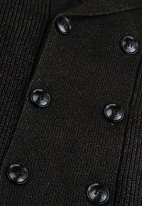 Czarna dzianina prążkowana z sześcioma połyskującymi czarnymi guzikami, charakteryzująca się teksturowaną powierzchnią i subtelnymi refleksami, podkreślającymi strukturę ubrania.