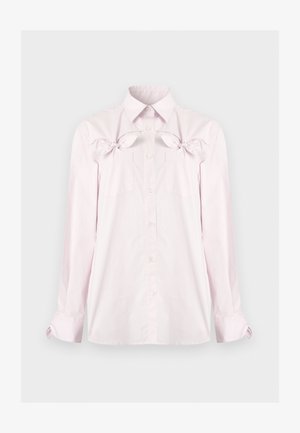 Világos rózsaszín, hosszú ujjú, gombos ing hegyes gallérral, mellzsebekkel és dekoratív masnikkal a zsebek felett, sima háttér előtt.
