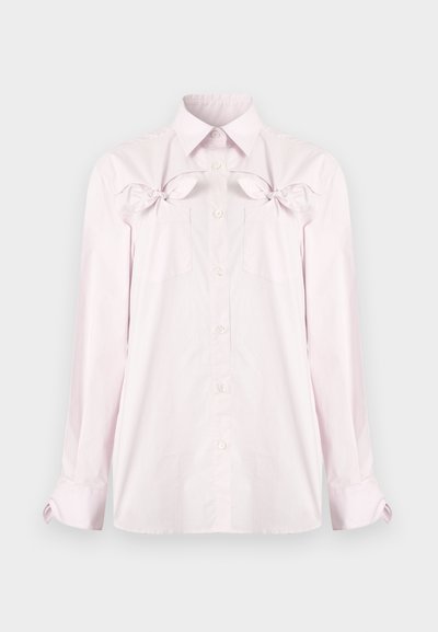 Chemise rose clair à manches longues avec boutons, col pointu, poches poitrine et nœuds décoratifs au-dessus des poches sur un fond uni.