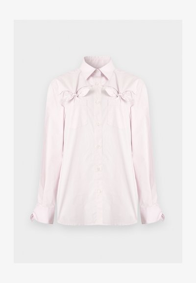 Chemise rose clair à manches longues avec boutons, col pointu, poches poitrine et nœuds décoratifs au-dessus des poches sur un fond uni.