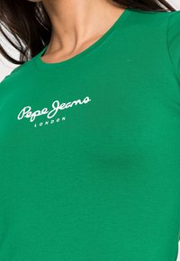 Grünes T-Shirt mit kurzen Ärmeln aus weichem Baumwollmaterial und Rundhalsausschnitt. Mit dem weißen "Pepe Jeans" Logo und dem Text "LONDON" als Akzenten.