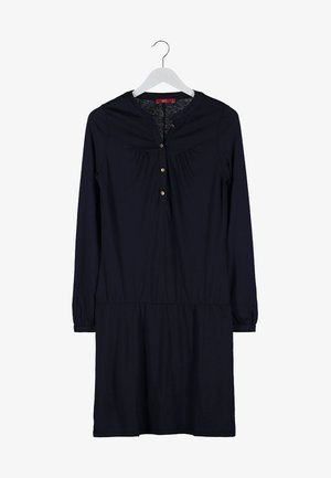 Femme portant une robe bleu marine à boutons, des collants noirs, des talons noirs et un sac à main noir avec une bandoulière en chaîne argentée.
