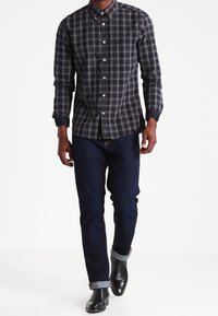 Camicia a quadri nera e grigia, slim fit, maniche lunghe. Indossata con jeans blu scuro e stivali neri in pelle alla caviglia, con i polsini arrotolati visibili.
