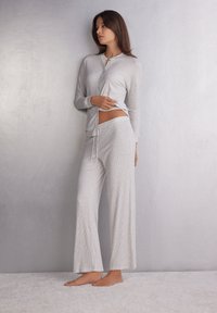Lichtgrijze geribde lounge-outfit bestaande uit een bovenstuk met lange mouwen en knopen en een broek met wijde pijpen en een koord in de taille. Zachte textuur, casual pasvorm.