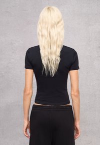 Top negro de manga corta ajustado, hecho de tela suave, combinado con pantalones negros de corte holgado. El cabello cae más allá de los hombros, con textura ondulada.