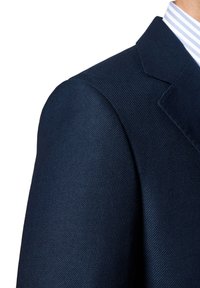 Granatowa marynarka z teksturowanej tkaniny, z kołnierzem z klapami i wyraźnie zarysowanymi ramionami. Widać fragment jasnoniebieskiej koszuli w paski znajdującej się pod spodem.