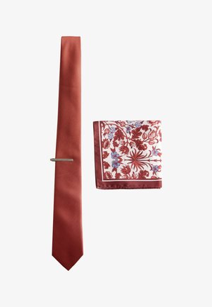 Rote strukturierte Krawatte mit silberner Krawattenklammer neben einem gefalteten weißen Einstecktuch mit roten und blauen Blumenmustern und einem roten Rand.