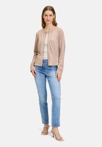 Ljusbeige mockajacka med rund halsringning, dragkedjestängning och två framfickor, kombinerad med ljusblå jeans och beiga sandaletter med remmar.