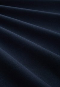Dunkelblauer Stoff mit weicher Textur, der glatte, gefaltete Drapierungen aufweist, die Tiefe und einen subtilen Glanz erzeugen.