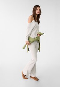 Světle šedá svetr bez ramene, bílá košile pod ním, v kombinaci se světle šedými kalhotami do zvonu. Zelený svetr uvázaný kolem pasu, hnědé tenisky.