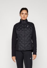Black athletic jacket with a quilted front, high collar, and long sleeves. Features a zip closure and side panels. Worn with black leggings.