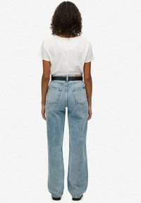 Lichtblauwe high-waisted jeans met een relaxte pasvorm, voorzien van gestikte achterzakken, een zwarte riem en een eenvoudige witte top met korte mouwen.
