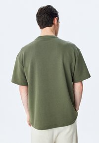 Olivengrøn kortærmet t-shirt i afslappet pasform, med en rund halsudskæring og minimale syninger ved kanten og ærmerne.