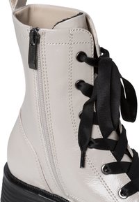 Botín de cuero charol gris claro con cordones negros, costuras en zigzag, cremallera lateral y suela exterior negra texturizada.