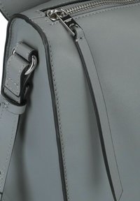 Borsa a tracolla in pelle grigia con texture liscia, hardware argentato, chiusura a zip e tracolla regolabile con cuciture dettagliate.
