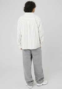 Chemise rayée en blanc cassé et gris clair, avec une coupe décontractée, fermeture à boutons et manches retroussées. Associée à un jean gris ample et des baskets.
