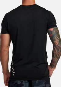 Zwarte sport T-shirt met korte mouwen, zachte textuur, zijlogo in het wit en een aansluitend ontwerp. Zichtbare tatoeage op de arm.