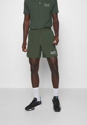 Man draagt een donkergroen EA7 Emporio Armani poloshirt en bijpassende korte broek, witte sokken en zwarte sportschoenen met blauwe accenten.
