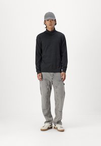 Mørkeblå langærmet skjorte med høj krave, parret med lysegrå cargo bukser og hvide sneakers, der har beige detaljer. En grå kasket fuldender looket.