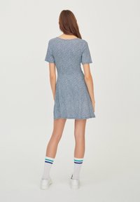 Krátké modré šaty s malým bílým květinovým vzorem, kulatým výstřihem a krátkými rukávy. Délka nad kolena, mírně rozšířená sukně.