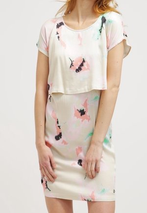 Femme portant une robe à manches courtes à motif floral pastel avec une couche supérieure courte et ample sur une jupe ajustée.