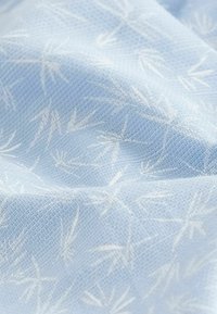 Lyst blå stof med et subtile hvidt mønster af bambusblade, lavet af et tekstureret materiale med en blød, glat overflade.