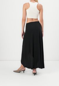 Jupe maxi noire à la coupe fluide avec une taille élastique, associée à un crop top blanc ajusté et des escarpins slingback beige.