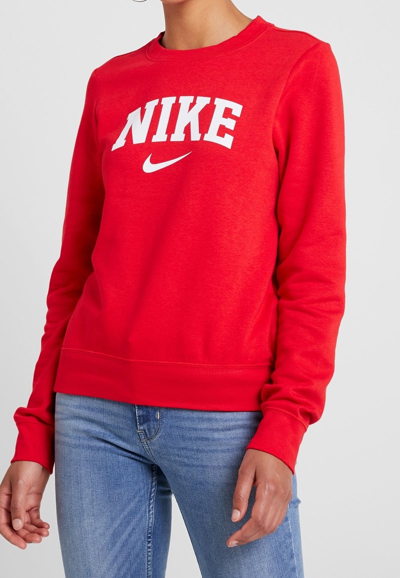 Röd sweatshirt i bomullsblandning med en vit "NIKE"-logga och swoosh. Ribbstickade muddar och fåll ger textur och struktur.