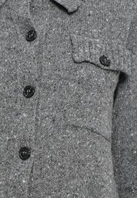 Szary dziany kardigan z czarnymi guzikami oraz kieszenią na piersi z klapką zapinaną na guzik.