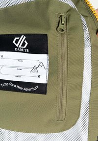 Grüner Stoff-Rucksack mit einem Reißverschluss, der ein schwarzes Etikett mit weißen Schriftzügen und Berggrafiken zeigt, akzentuiert durch weißes Netz und einen bunten Reißverschluss.