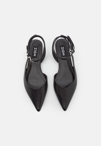 Zapatos slingback de cuero negro con diseño de punta afilada, que cuentan con una delgada correa en el tobillo y una textura suave. Logo mostrado en la suela interior.