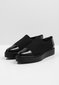 Černé nazouvací boty s lesklou špičkou a silnou plochou podrážkou, na boku podrážky s logem Calvin Klein.