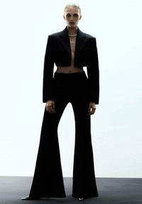 Blazer noir court avec revers à encolure, associé à un pantalon évasé taille haute noir assorti. Texture lisse, design minimaliste.