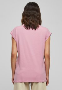 Pink short-sleeved t-shirt with a relaxed fit, smooth texture, and rolled cuff detailing. Simple back design with no visible embellishments.