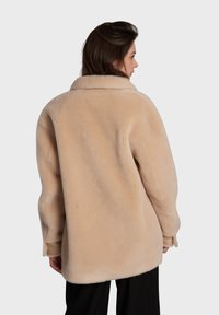 Casaco de pele sintética bege com um colarinho largo, corte oversized e mangas longas. Apresenta uma textura suave e um design minimalista.