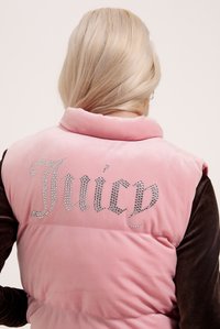 Ružičasti baršunasti prsluk s visokim ovratnikom i crnim rukavima, sa slovima "Juicy" od rhinestona na leđima. Mekana tekstura i sjajni detalji.