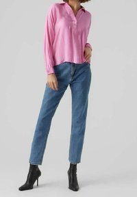 Różowa bluzka z długim rękawem i kołnierzykiem, zapinana na guziki, w połączeniu z niebieskimi dżinsami z wysokim stanem i czarnymi botkami na obcasie.