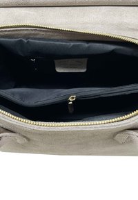 Interno di una borsa in suede beige con fodera nera. Presenta una zip dorata e un piccolo scomparto con zip per l'organizzazione.