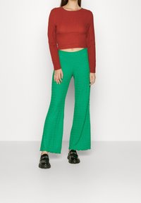 Pullover rosso cropped con tessuto testurizzato, abbinato a pantaloni verde con gamba a zampa di elefante e orlo ondulato. Mocassini neri chunky completano il look.